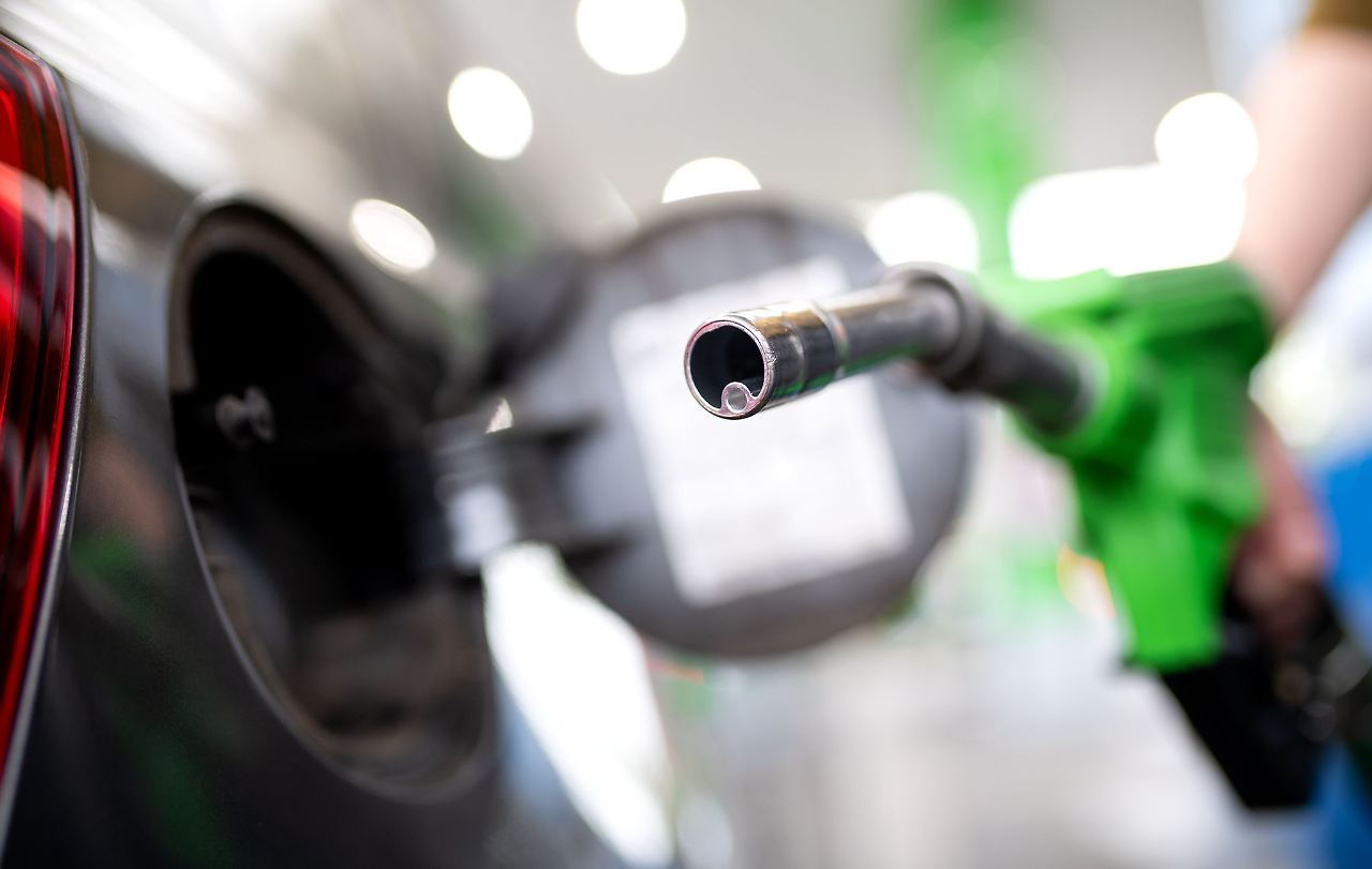 Eine Hand führt eine Zapfpistole an einer Tankstelle zur Tanköffnung