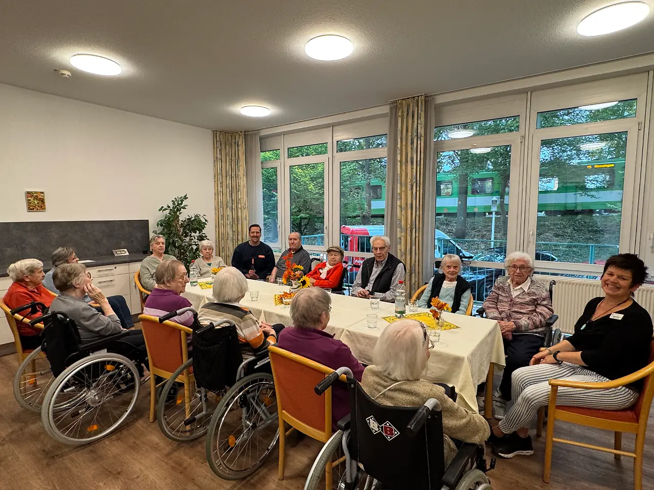 Eine Gruppe älterer Menschen sitzt um einen Tisch in einem Gemeinschaftsraum.