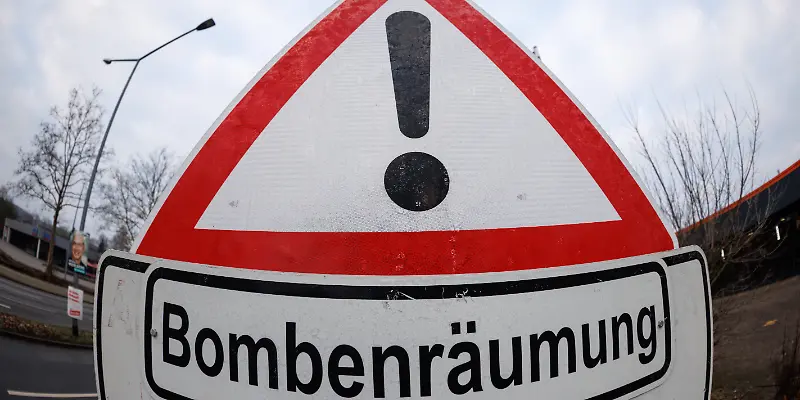 Ein Warnschild mit einem Ausrufezeichen und dem Text "Bombenräumung" steht am Straßenrand.