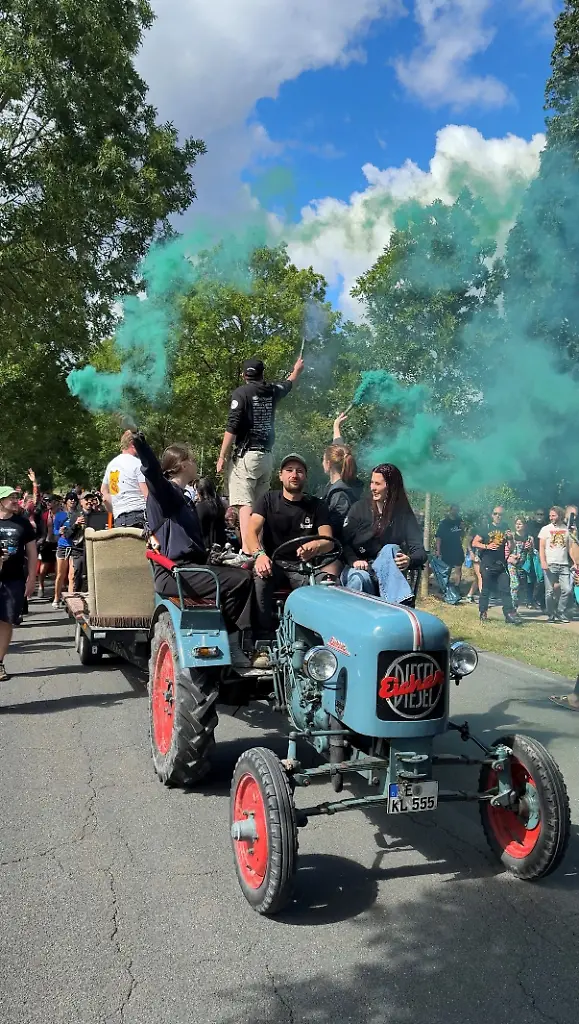 Eine Gruppe von Menschen fährt auf einem Traktoranhänger und schwenkt grüne Rauchfackeln.