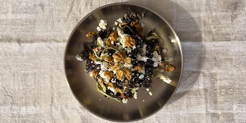 Ein Salat mit Grünkohl, Walnüssen und Feta in einer Metallschüssel auf einem Tisch. Ein Salat mit Grünkohl, Walnüssen und Feta in einer Metallschüssel auf einem Tisch.